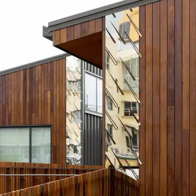 The modern building, part of Taranaki Hospital, boasts a wooden exterior with mirrored sections reflecting the surrounding architecture, creating a harmonious blend with its urban environment.