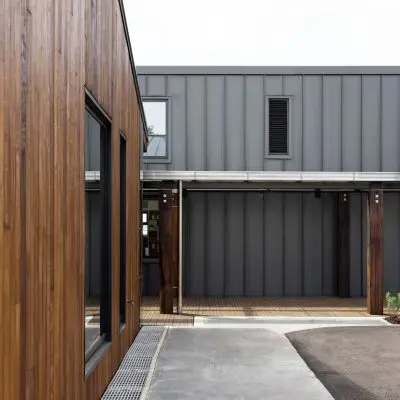 The modern building exterior, reminiscent of the new Taranaki Hospital design, boasts wood and metal cladding with expansive windows that illuminate an open central courtyard.