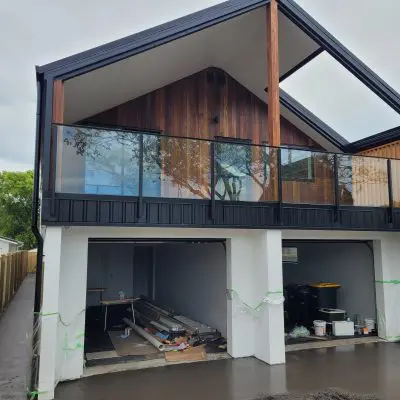 A modern two-story house featuring Australian Timber accents with sleek wood and black paneling. The glass balcony adds elegance, while the open garage brims with NSW Spotted Gum construction materials, capturing a blend of style and substance.