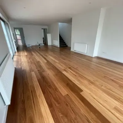 The room features solid wooden floors, white walls, a staircase, and a sliding glass door. Engineered radiators are mounted on the walls.