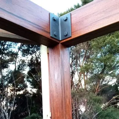 Timber beams and posts connected by a metal bracket with bolts, set against a backdrop of trees and sky.