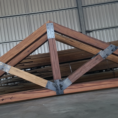 A hand-brushed wooden truss structure with metal joints is artfully displayed in a warehouse setting.