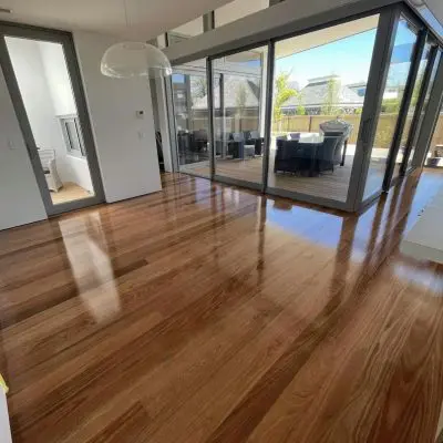 Spacious room with polished, engineered wooden flooring, large glass doors leading to an outdoor patio with seating, and ample natural light.