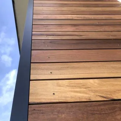 Close-up of a Spotted Gum wooden wall with horizontal panels and visible screws, framed by a sleek black metal edge, set against the vibrant blue sky of NSW.