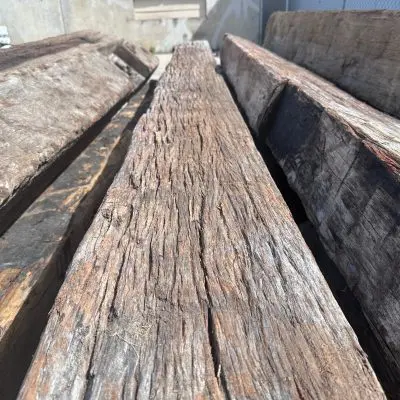 Close-up of large, aged wooden beams stacked together outdoors, showcasing the natural state hardwood's texture and grain.